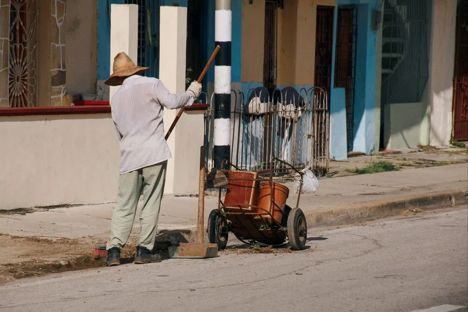A man in a blue t-shirt cleaning large glass pane with a squeegee indoors.
